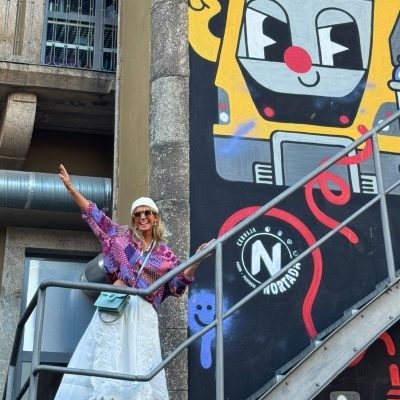 Mulher com roupa colorida em escadas metálicas junto a mural com comboio animado e texto NORTE