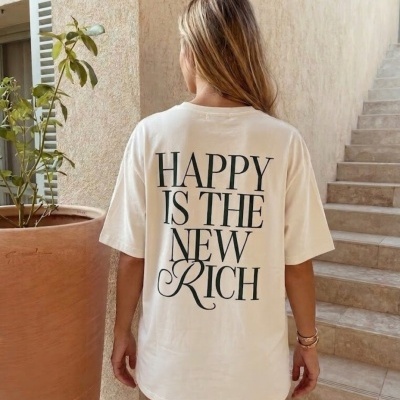 T-shirt branca com texto preto HAPPY IS THE NEW RICH nas costas, vista de costas.