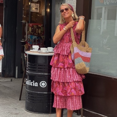 Mulher com vestido rosa, sandálias vinhas, lenço na cabeça e bolsa de crochê numa rua urbana