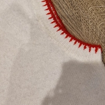 Peça branca de tecido macio com borda vermelha sobre madeira