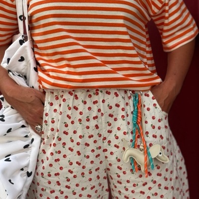 Conjunto casual com t-shirt às riscas laranja e branco e calças creme com padrão de cerejas
