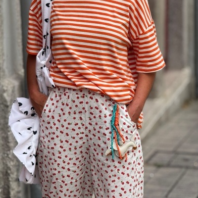 T-shirt laranja às riscas com calças brancas estampadas com cerejas e bolsa branca com corações pretos