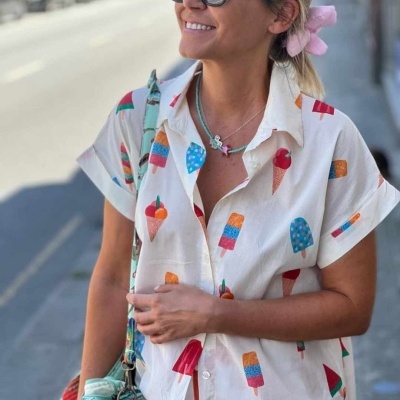 Camisa branca com estampado de gelados coloridos, mulher com óculos de sol e acessórios coloridos na rua