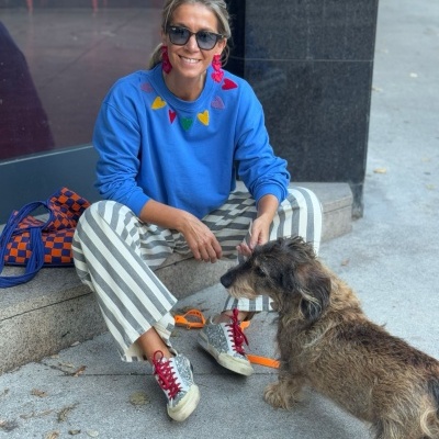 Mulher com sweat azul, calças às riscas, ténis brancos e cão castanho de pelo comprido