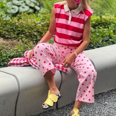 Mulher sentada com camisola riscada rosa e vermelha, calças cor-de-rosa com bolinhas vermelhas, óculos e chinelos amarelos