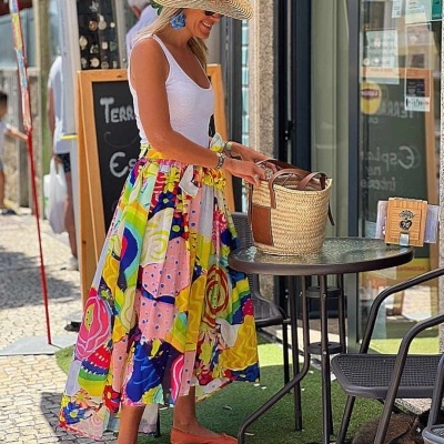 Mulher com vestido colorido, chapéu de palha e mala de palha numa esplanada