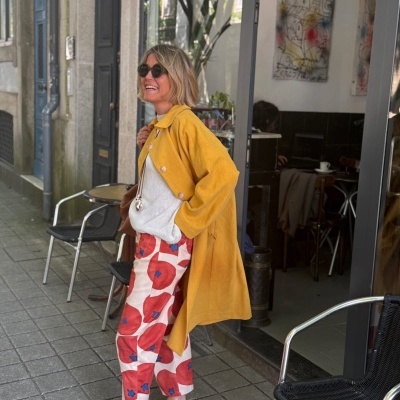 Mulher com casaco amarelo e calças estampadas em passeio urbano junto a café