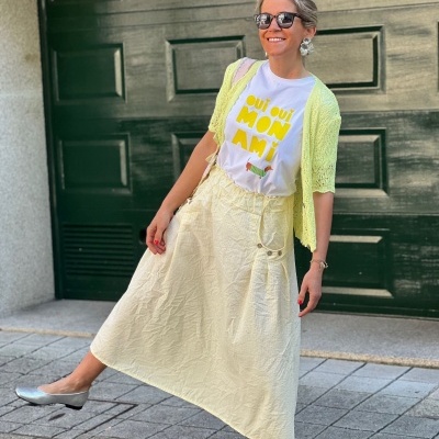 Mulher com roupa casual colorida e óculos escuros em frente a uma porta verde escura.