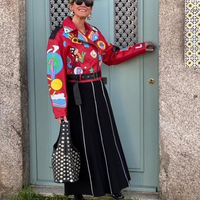 Pessoa com jaqueta vermelha colorida e saia preta em frente a porta azul