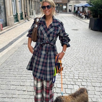 Mulher de casaco e calças xadrez a passear o cão numa rua empedrada urbana