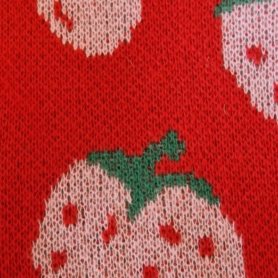 Tecido de malha vermelho com padrão rosa de morangos e cerejas com folhas verdes.