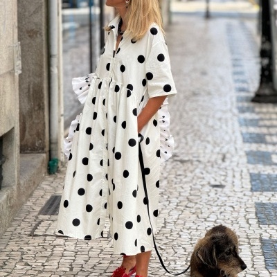 Mulher com vestido branco de bolinhas pretas e sandálias vermelhas a passear cão pequeno na rua