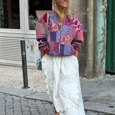 Mulher com casaco patchwork colorido e saia branca numa rua de calçada portuguesa