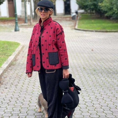 Mulher com casaco rosa com bolinhas pretas, calças pretas e boné numa rua pavimentada