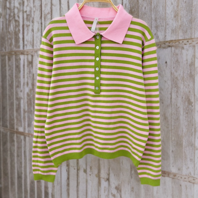 Camisola de riscas rosa e verde com gola de polo rosa pendurada num cabide de madeira