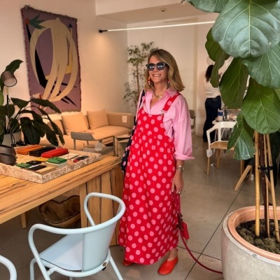 Mulher com vestido vermelho de bolas cor-de-rosa, camisa rosa e óculos escuros em interior decorado