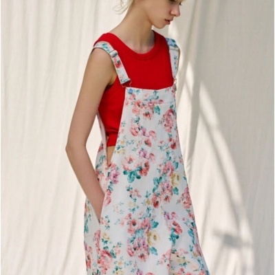 Vestido jardineira floral branco com t-shirt vermelha sem mangas e fundo neutro.