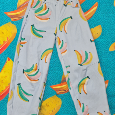 Calças claras com padrão colorido de bananas sobre fundo azul com bananas.
