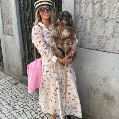 Mulher com vestido com padrão de cães estampados segurando cão peludo castanho e preto