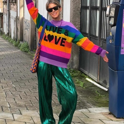 Mulher com camisola colorida com o texto LIVE & LOVE e calças verdes metalizadas na rua junto a máquina azul.