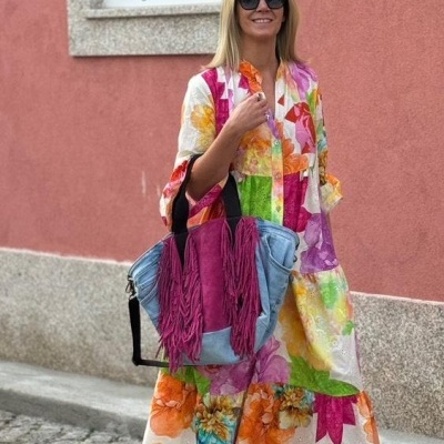 Mulher com vestido de flores coloridas e mala rosa azul com franjas