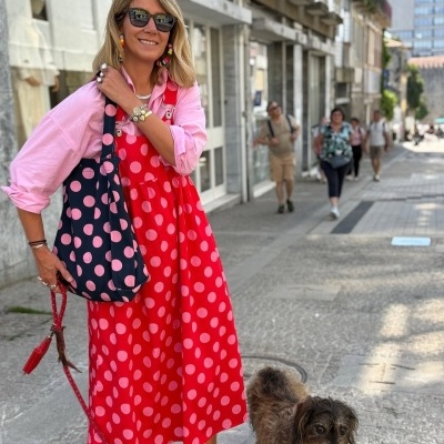 Mulher com vestido vermelho de bolinhas e bolsa azul de bolinhas a passear cão numa rua