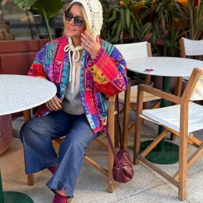 Mulher sentada em esplanada com casaco colorido acolchoado e acessórios de inverno.