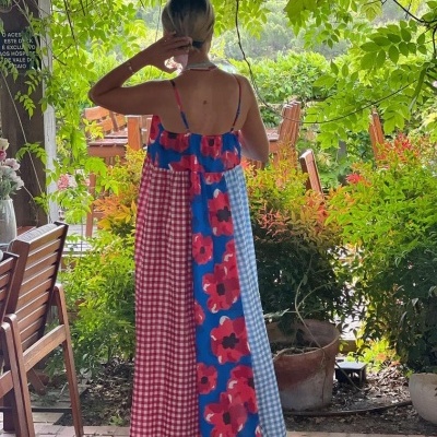 Mulher de costas com vestido colorido em padrão xadrez e floral num jardim exterior
