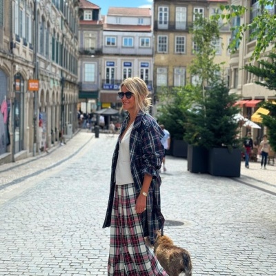 Pessoa com roupa xadrez e óculos escuros a passear com cão numa rua de calçada entre edifícios antigos