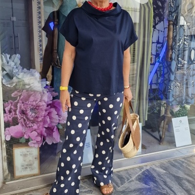 Mulher com blusa azul escura, calças azul com bolinhas brancas, sandálias e bolsa de palha