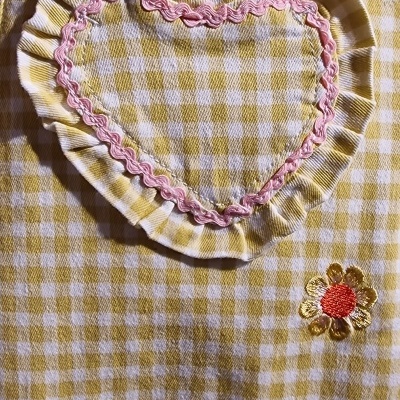 Detalhe de tecido xadrez amarelo e branco com bolso em forma de coração e bordados de flores