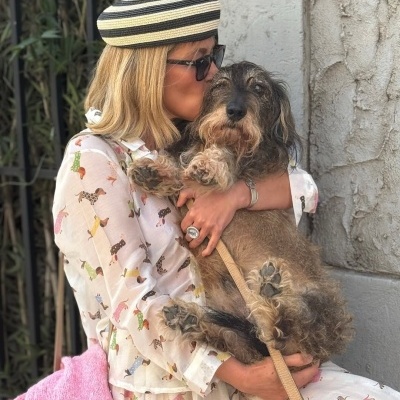Camisa branca com padrão de cães coloridos sendo usada por mulher a segurar um cão peludo castanho