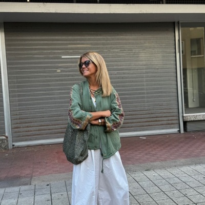 Mulher com blusa verde e calças brancas em frente a porta metálica com letreiro GARAGEM