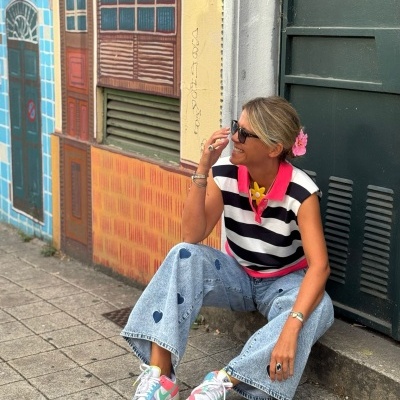 Mulher sentada com roupa casual colorida e óculos escuros junto a porta verde e mural colorido