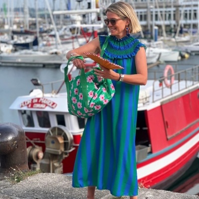 Mulher em vestido riscas azuis e verdes com mala floral junto a barcos no porto