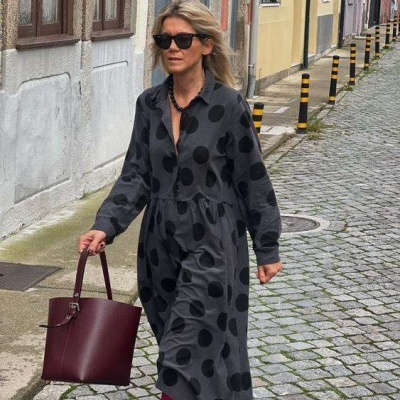 Vestido cinza escuro com bolinhas pretas e acessórios granada em rua de calçada de pedra