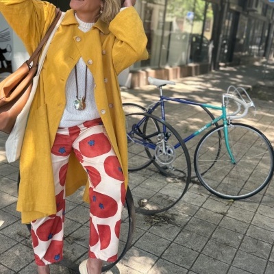 Mulher com casaco amarelo e calças estampadas ao lado de bicicleta