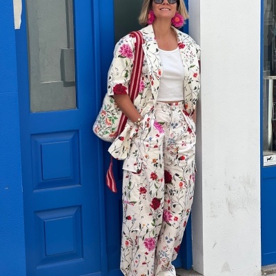 Mulher com fato floral, óculos escuros e brincos cor-de-rosa junto a uma porta azul.