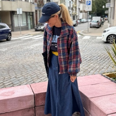 Mulher com roupa colorida e boné numa rua urbana com calçada de pedras