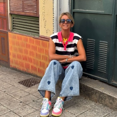 Mulher sentada na rua com calças de ganga azuis com corações, t-shirt às riscas e sapatilhas coloridas.