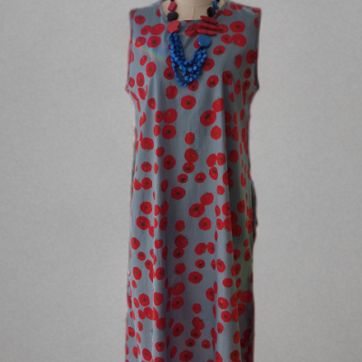 Vestido comprido cinzento com flores vermelhas e colar azul e vermelho num manequim.