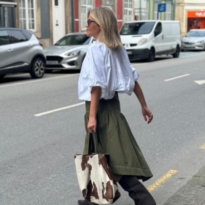 Mulher a andar na rua com saia verde e bolsa padrão pele de vaca.