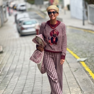 Mulher com camisola e calças riscas, óculos e chapéu a caminhar na rua