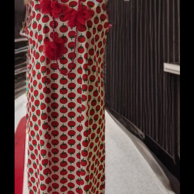 Vestido comprido branco com padrão de maçãs vermelhas num manequim, com colares vermelhos, em fundo de estrutura preta e chão cinzento.