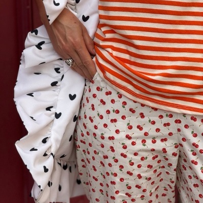 Camisola laranja às riscas brancas, calças brancas com cerejas vermelhas, saco branco com corações pretos e folhos