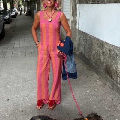 Mulher com conjunto rosa e laranja listrado, acessórios cor-de-rosa, óculos escuros, a passear cão na rua