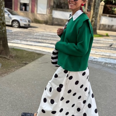 Mulher a usar saia branca com bolinhas pretas e casaco verde com gola branca
