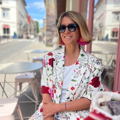 Mulher sentada ao ar livre com fato branco estampado, óculos de sol e brincos rosa