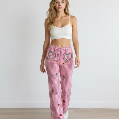 Modelo feminina com top branco e calças rosas xadrez com bordados coloridos