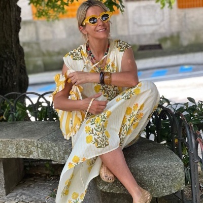 Mulher com vestido floral amarelo e óculos de sol amarelos sentada num banco de pedra